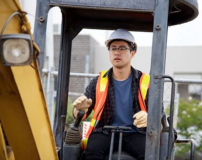 Man driving construction equipment wearing a hard hat and orange safety vest