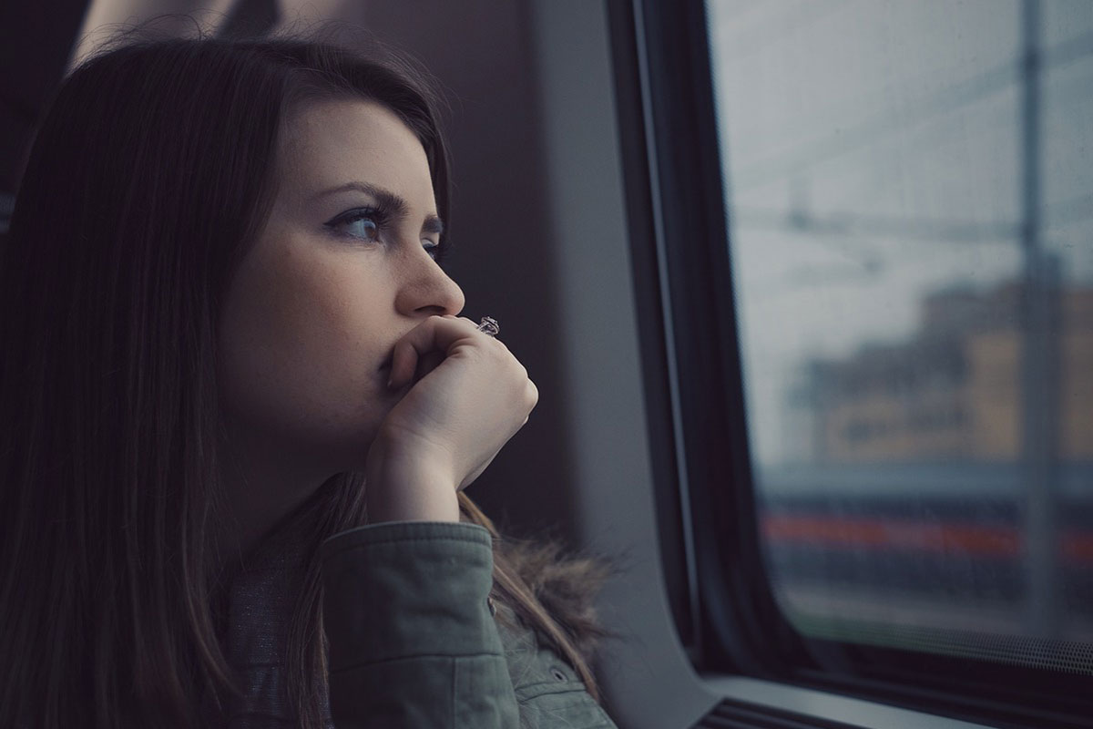 A woman looking out a train window with her chin resting in her hand.